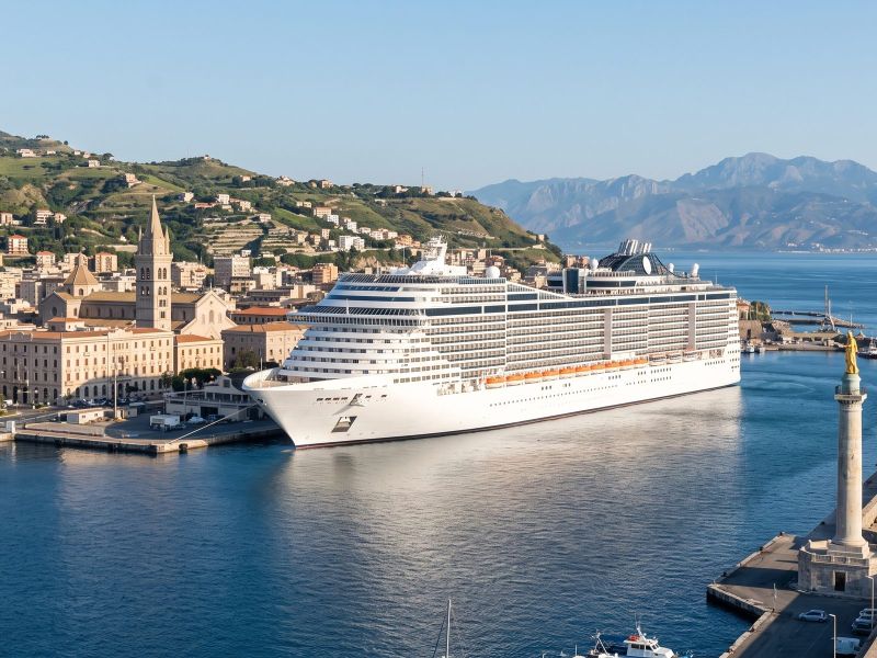 Groot modern cruiseschip aan de kade in het centrum van Messina, met de havenzuil en Calabrië aan de overkant van de zeestraat