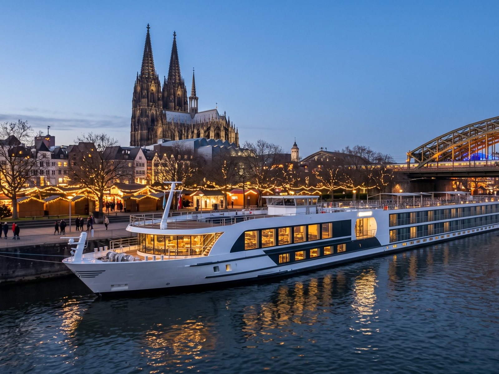 River cruise ship on the Rhine below Cologne Cathedral, with Christmas market lights along the riverbank