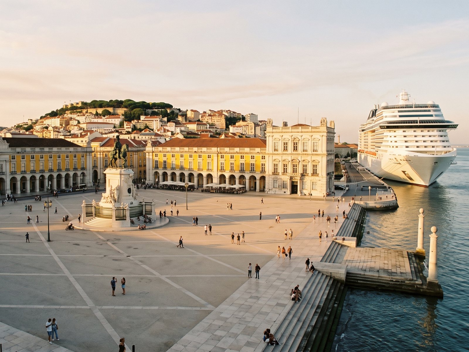 Praça do Comércio in Lisbon at golden hour, with a cruise ship moored along the river below Alfama