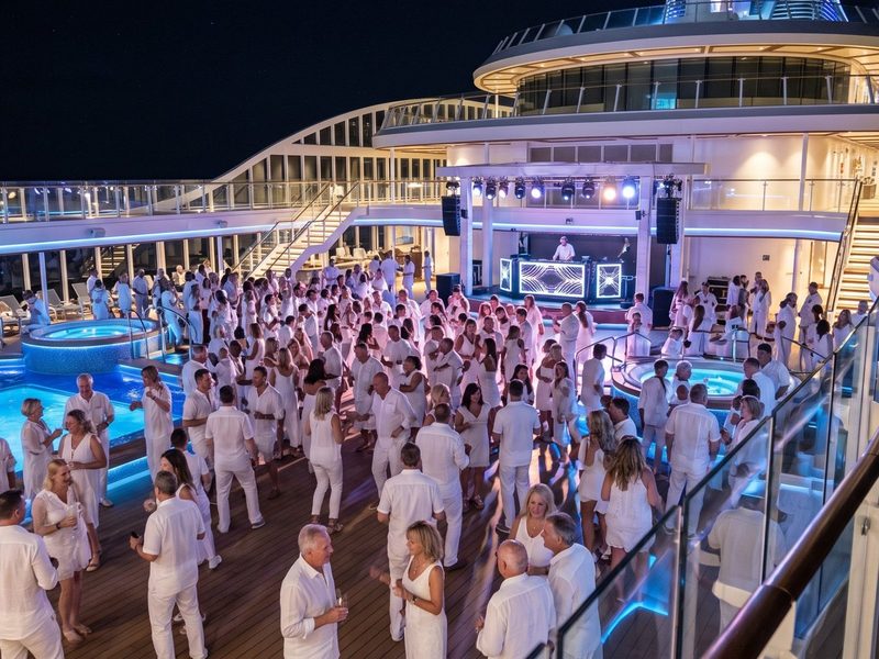 Huéspedes vestidos de blanco bailan en una fiesta en la cubierta abierta por la noche