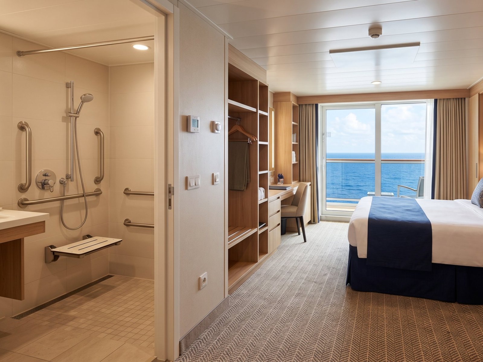 An accessible cruise cabin with a roll-in shower, grab rails, a fold-down seat and space next to the bed